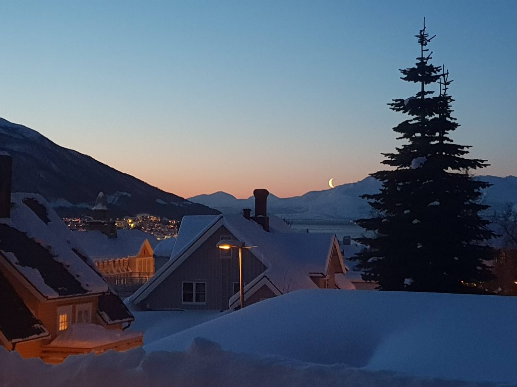 Paesino innevato al crepuscolo con falce di luna in cielo