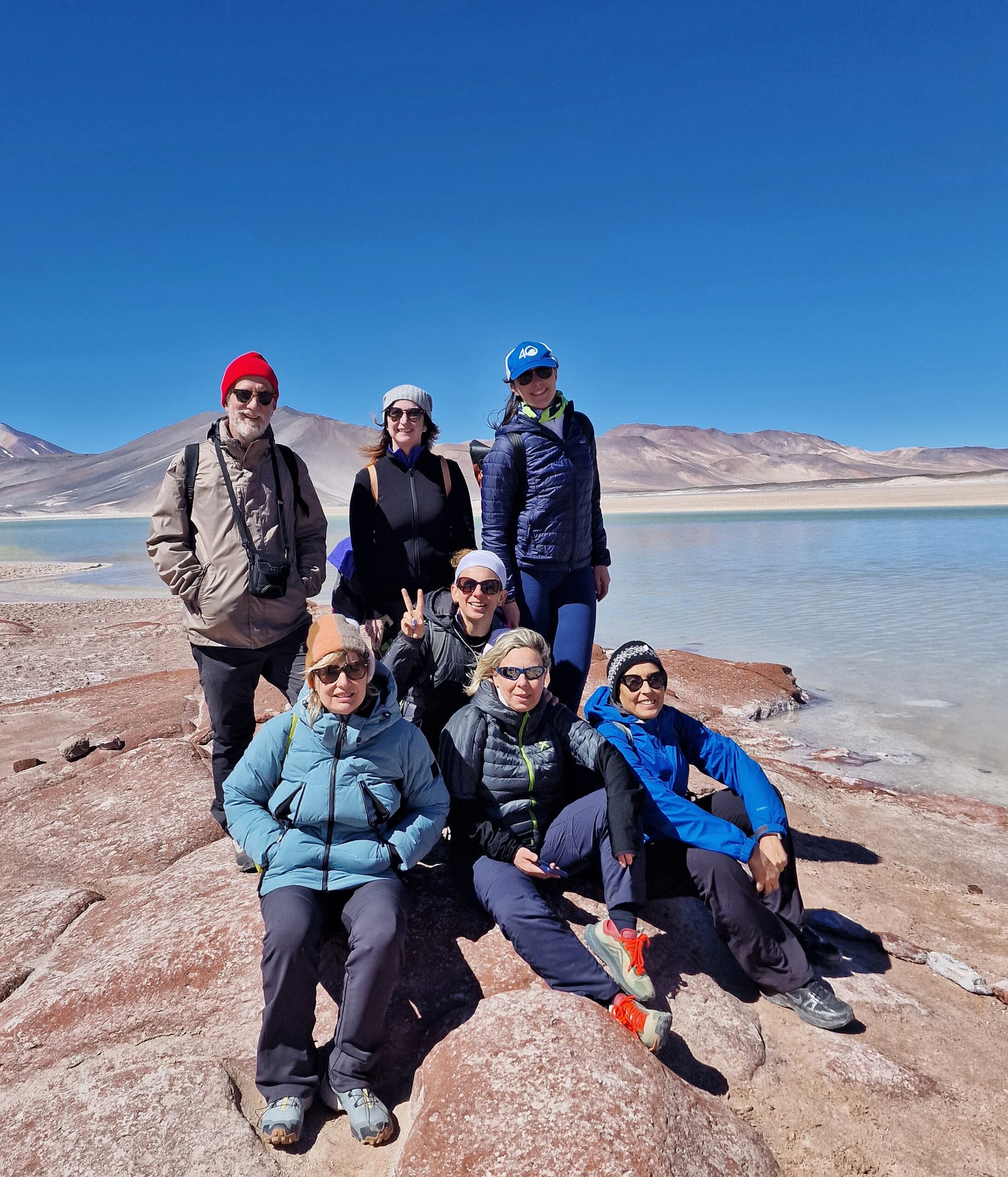 Gruppo di persone su rocce color sabbia, con lago sullo sfondo e cielo blu