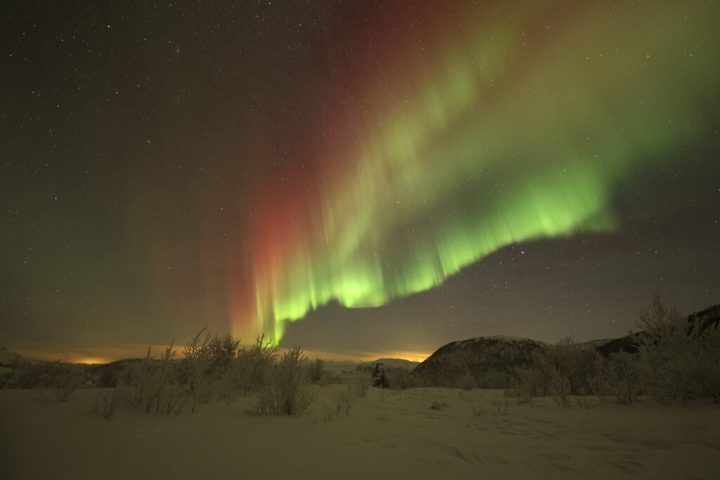 Aurora boreale rossa e verde con paesaggio innevato