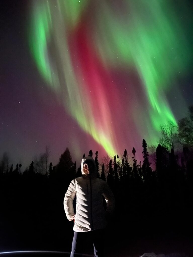 Persona di fronte in giacca a vento con aurora boreale verde e viola alle spalle