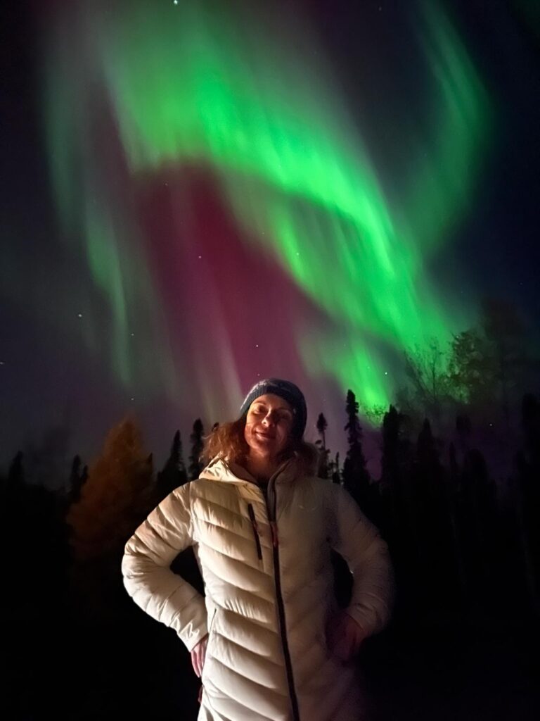 Persona di fronte in giacca a vento con aurora boreale verde e viola alle spalle